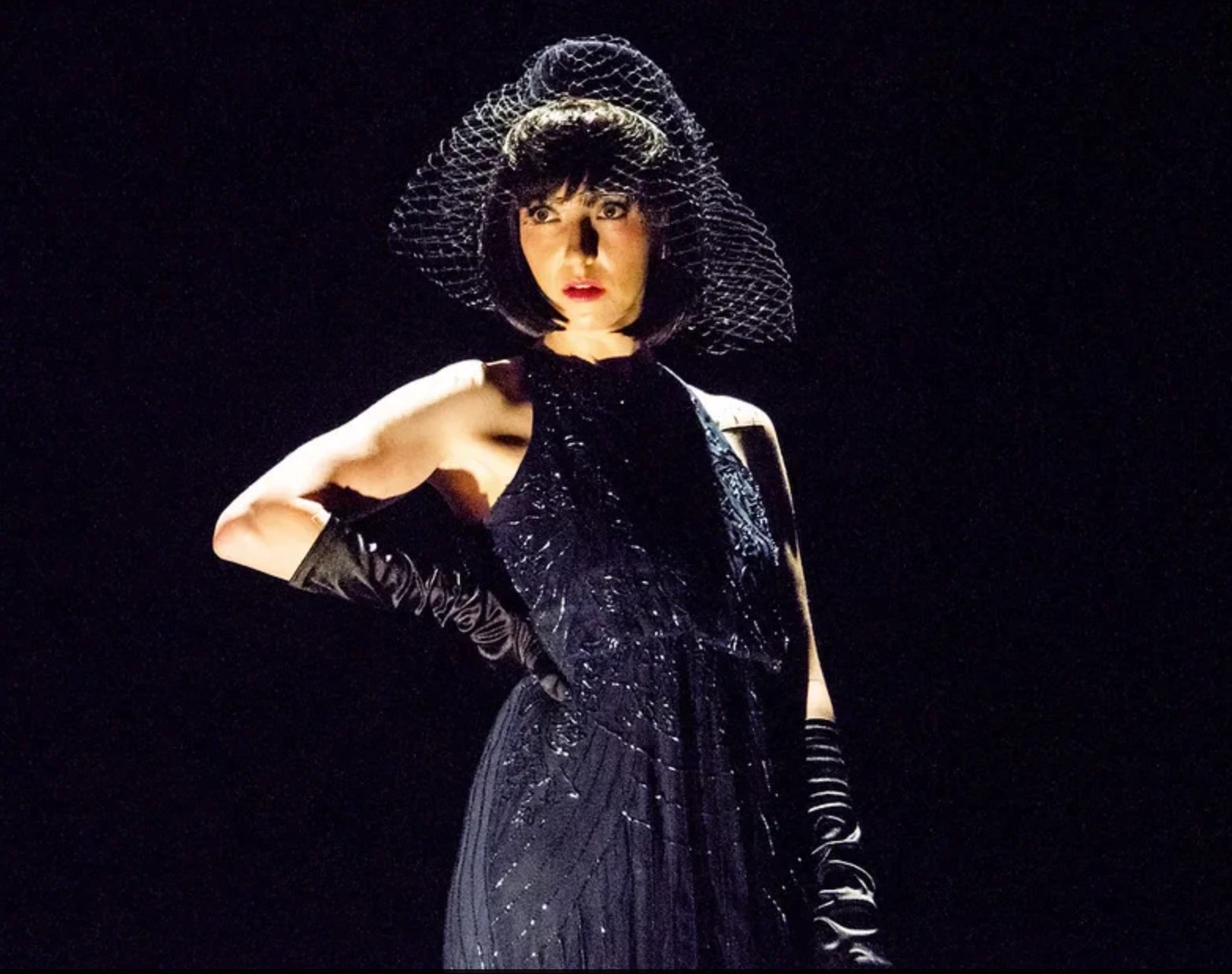 Annabella Schmidt in a veiled hat and long black gloves, in a single spotlight