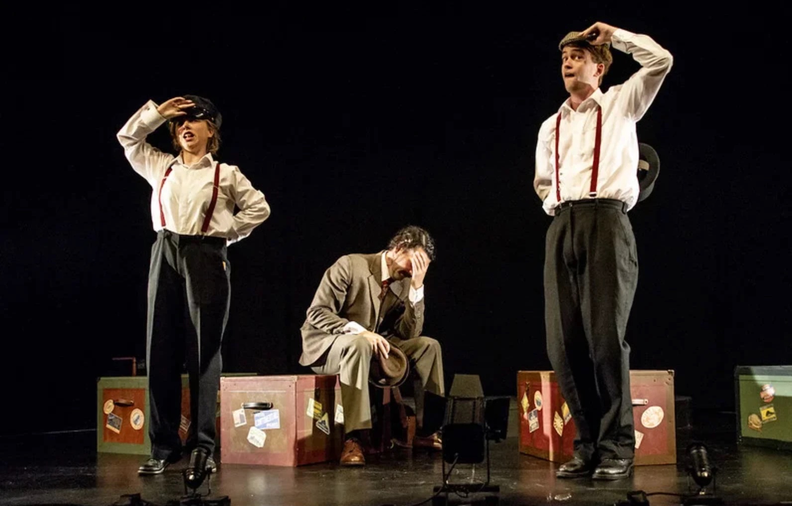 Two actors salute among luggage trunks while Hannay sits with his head in his hand