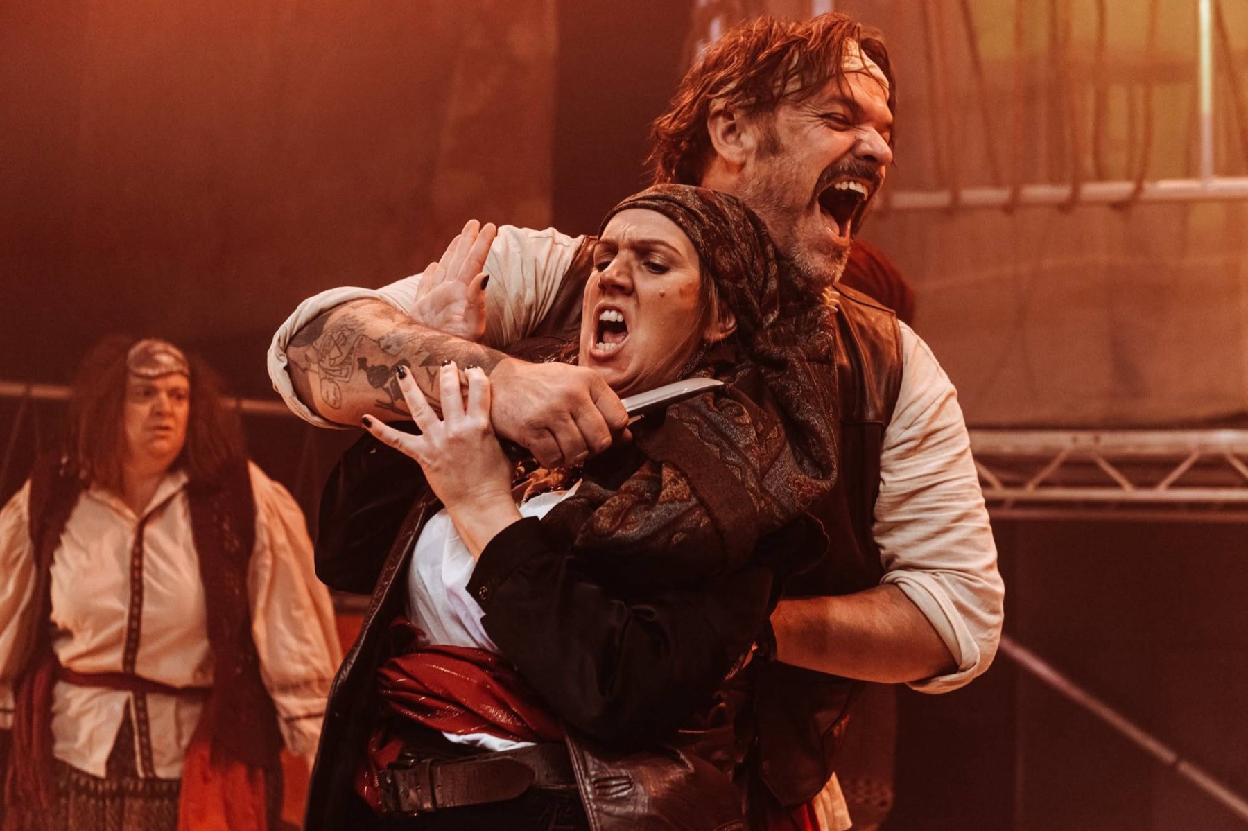 A pirate holds a knife to a woman's throat, both shouting
