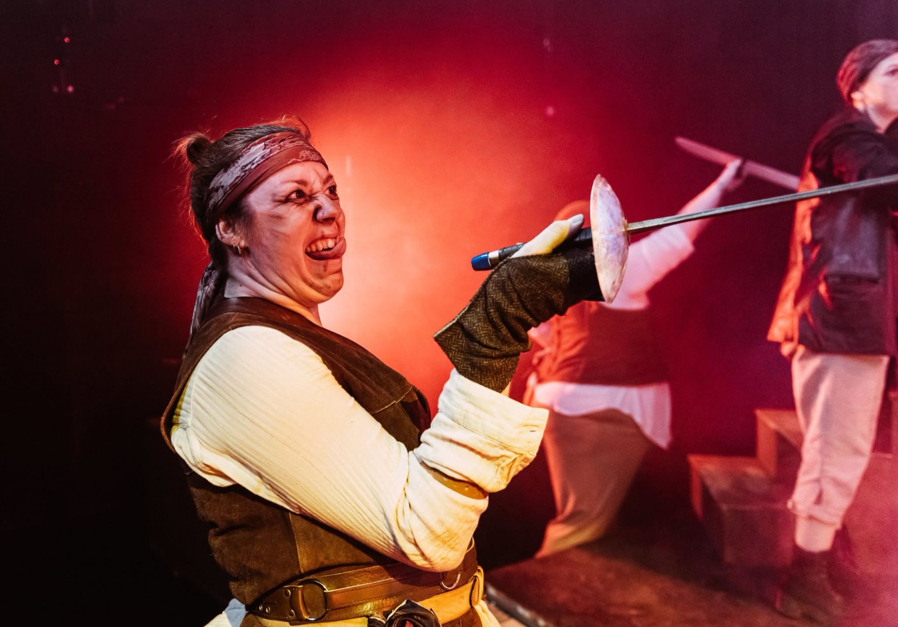 A pirate grimaces wildly along the blade of a sword in red light