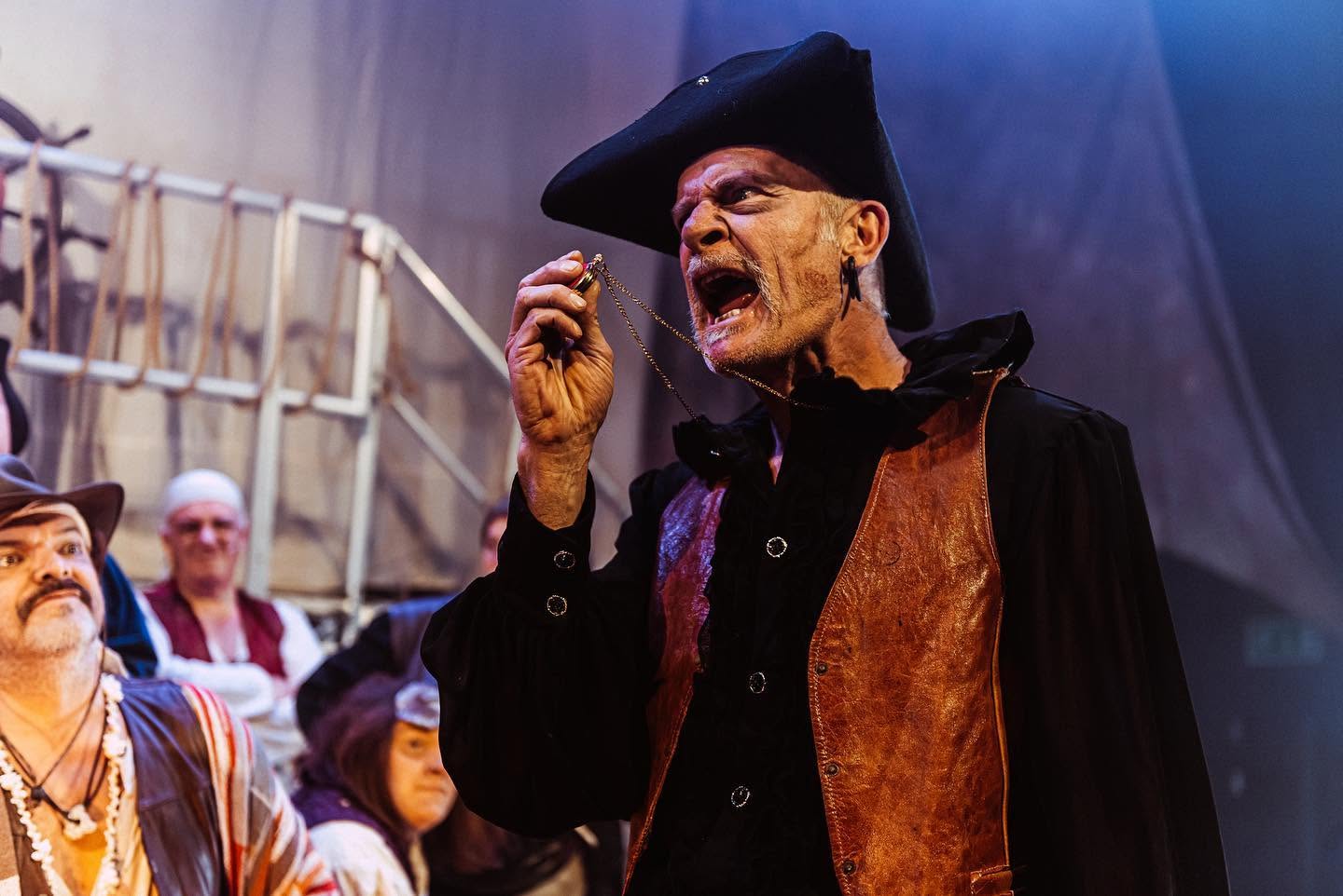 A pirate in a tricorn hat snarls, holding up a locket on a chain